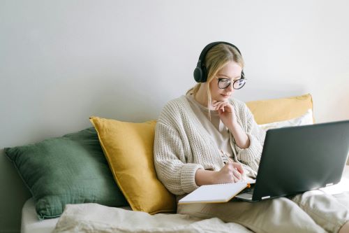 Woman with headphones on is sitting on a sofa while on a laptop